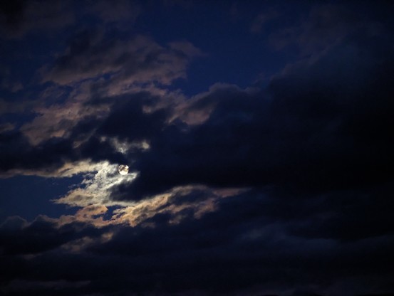 A photo of the night sky with clouds passing in front of a bright moon.