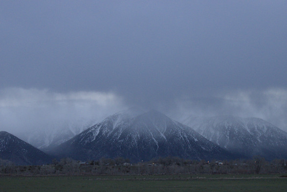 A photo of mountains being partially covered by snow clouds. The lighting is such that only parts of the sky are bright.