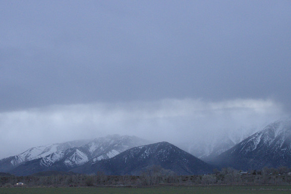 A photo of mountains being partially covered by clouds. You can see snow coming down from the clouds onto the mountains.